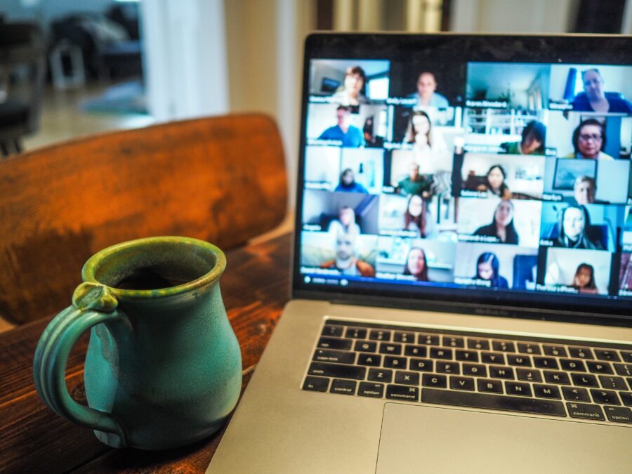 a mug and laptop screen on a wooden table. The laptop screen is displaying a group video call.